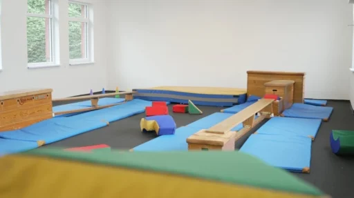 Blick in unsere Turnhalle in Schwerte. Spielgeräte liegen im Raum herum. Es sind verschiedenen Turngeräte zu einem Parcours aufgebaut. Um den Parcours herum liegen viele blaue Turnmatten.